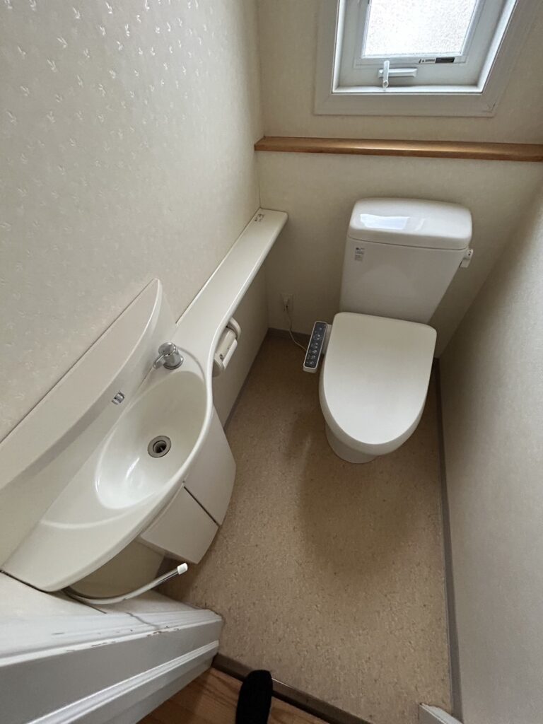 リフォーム前の1階トイレです。タンク付きトイレの横に独立した手洗いカウンターがあり、空間がやや手狭に感じられるレイアウトでした。こちらもお掃除のしやすさの改善が課題でした。