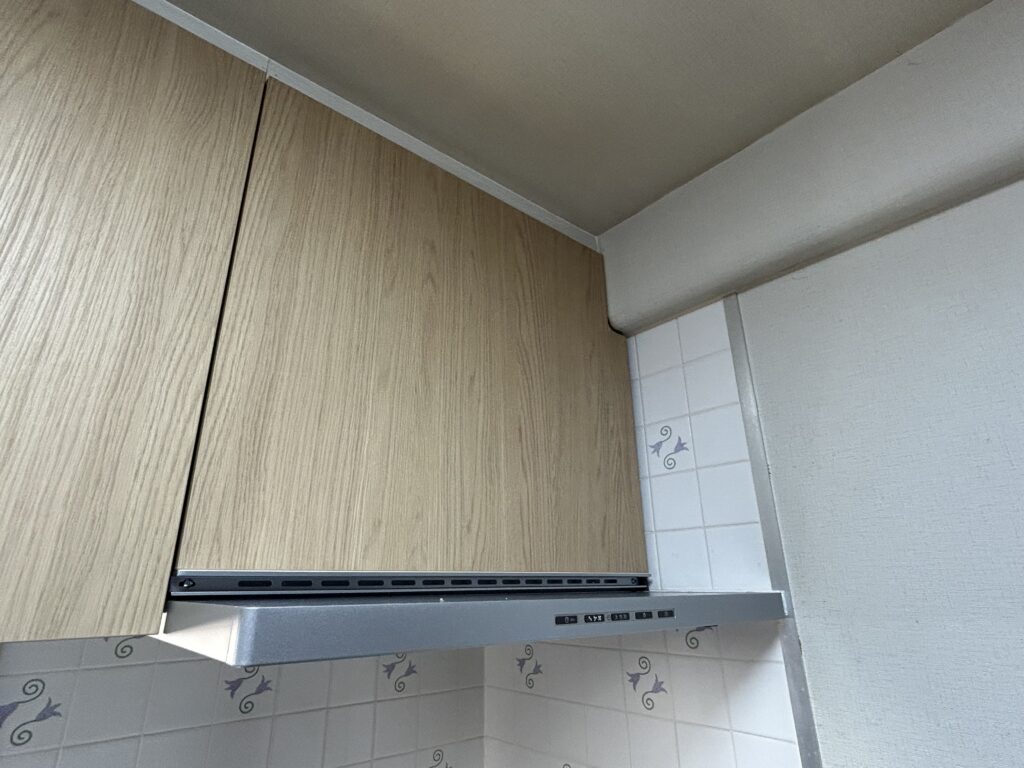 従来のブーツ型から、お手入れがしやすくスタイリッシュな薄型レンジフードに交換しました。圧迫感がなくなり、見た目もすっきり。吊戸棚もキッチン本体と統一することで、洗練された明るい空間を実現しました。<br />
