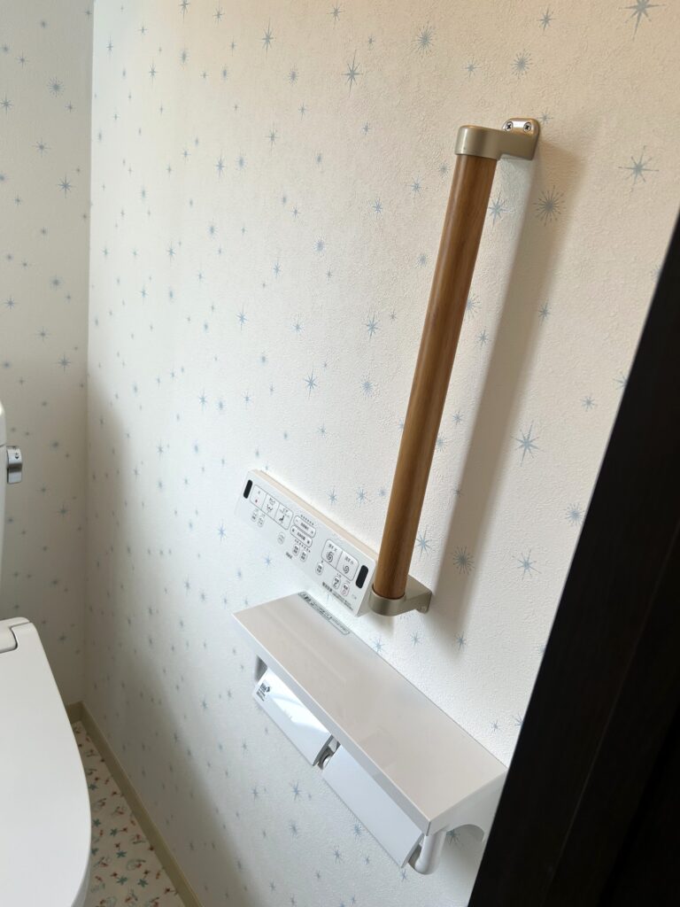 壁付けのスマートなリモコンで操作性が向上。立ち座りを補助する手摺も設置し、安全性を高めました。棚付きのペーパーホルダーは小物置きにも便利です。