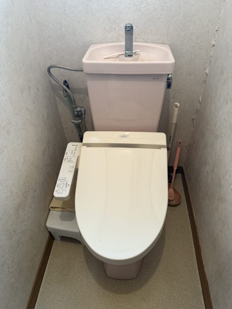 従来のトイレは、ピンク色の便器と手洗いタンクが経年変化で汚れやすく、床のクッションフロアも変色して暗い印象の空間でした。