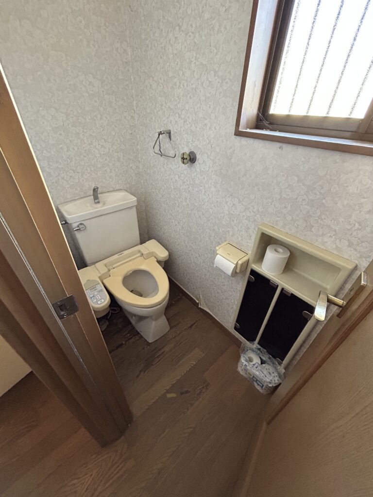 交換前の古い温水洗浄便座付きトイレは、便座部分の黄ばみが目立ち、手洗い付きタンクや壁紙クロスに落としきれない水垢が固着していました。